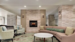 A modern living room with a fireplace, beige patterned walls, a beige sofa, two armchairs, and a coffee table.