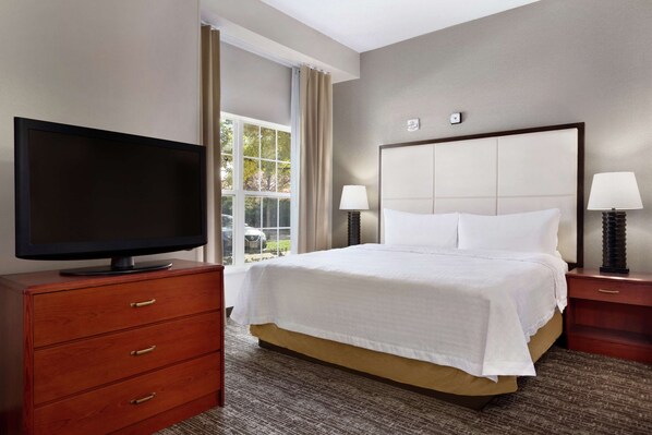 Habitación de hotel con una cama, un televisor sobre una cómoda de madera, dos lámparas de noche y una ventana con cortinas.