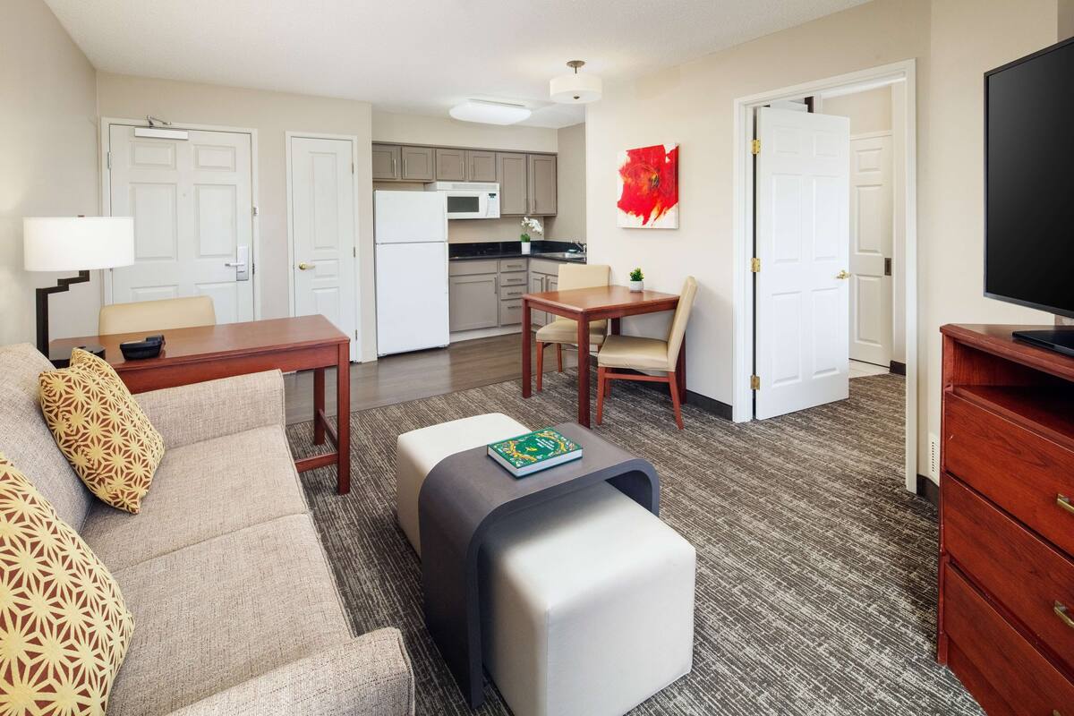 A compact living space with a sofa, a coffee table, a dining table, a kitchen area, and a television.