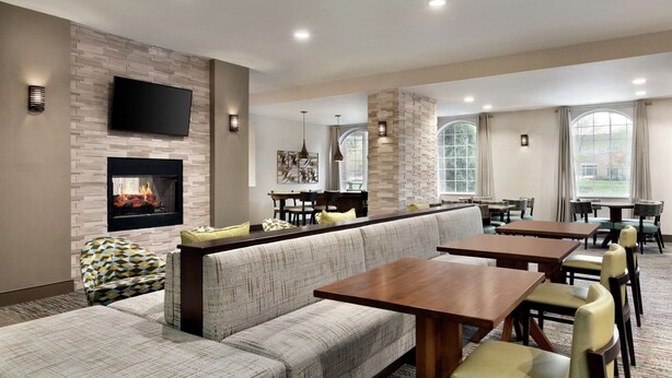 A modern hotel lobby with a fireplace, seating area, and dining tables.