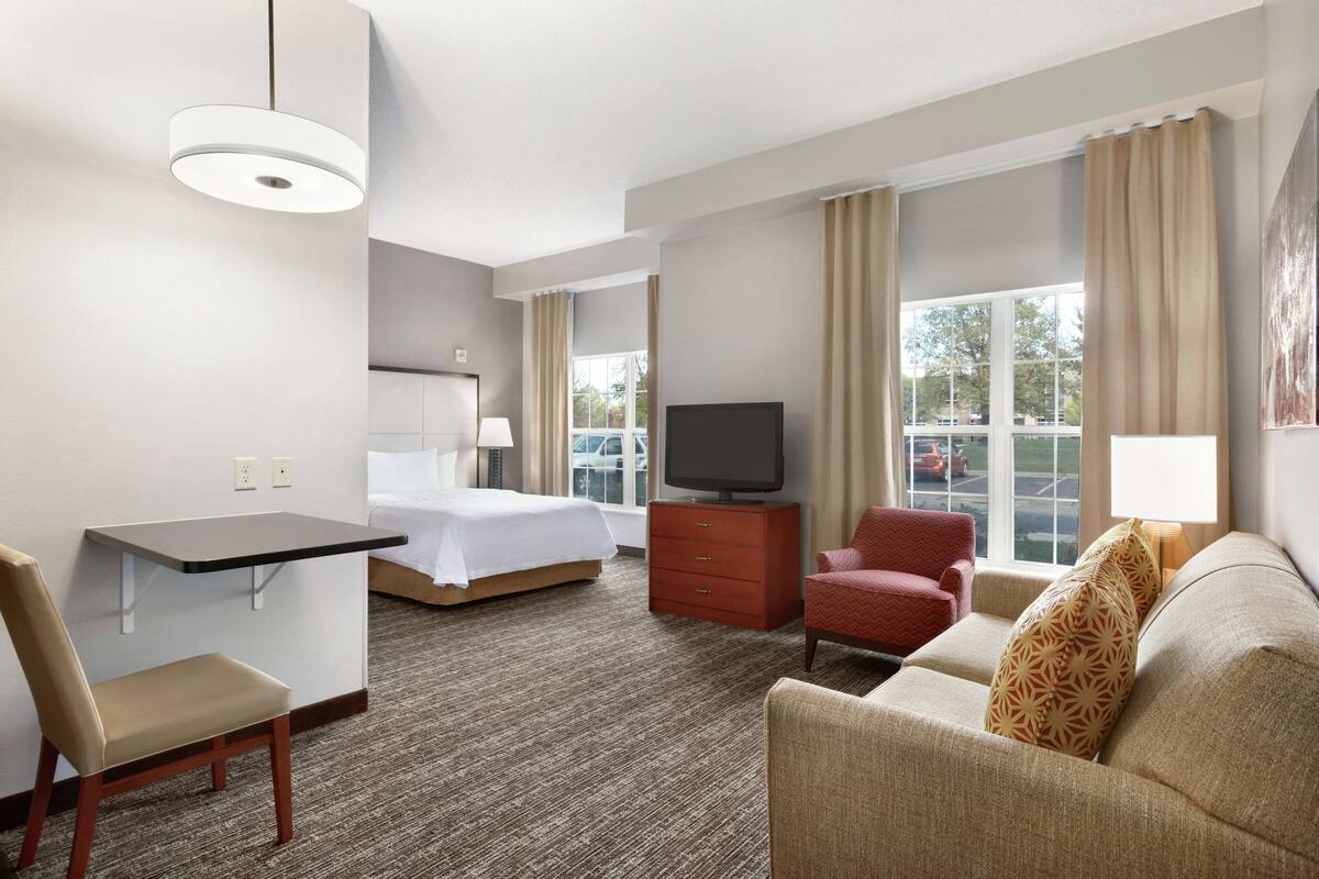 A hotel room with a bed, a desk, a TV, a sofa, and a chair.