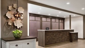 A hotel reception area with a modern design, featuring a reception desk, a decorative wall with large white flowers, and a white cabinet with a green apple bowl on top.