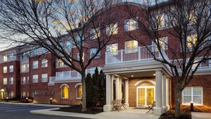 A multi-story brick building with a covered entrance and a bench outside.