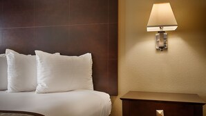 A hotel room with a bed, two pillows, a nightstand, and a wall-mounted lamp.