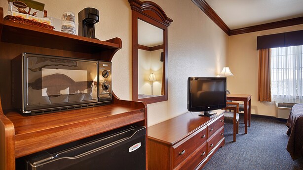 A hotel room with a wooden dresser, a microwave, a television, and a mirror.