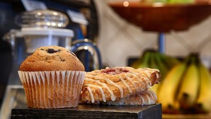 A muffin in a paper cup and a pastry with icing on a wooden surface.