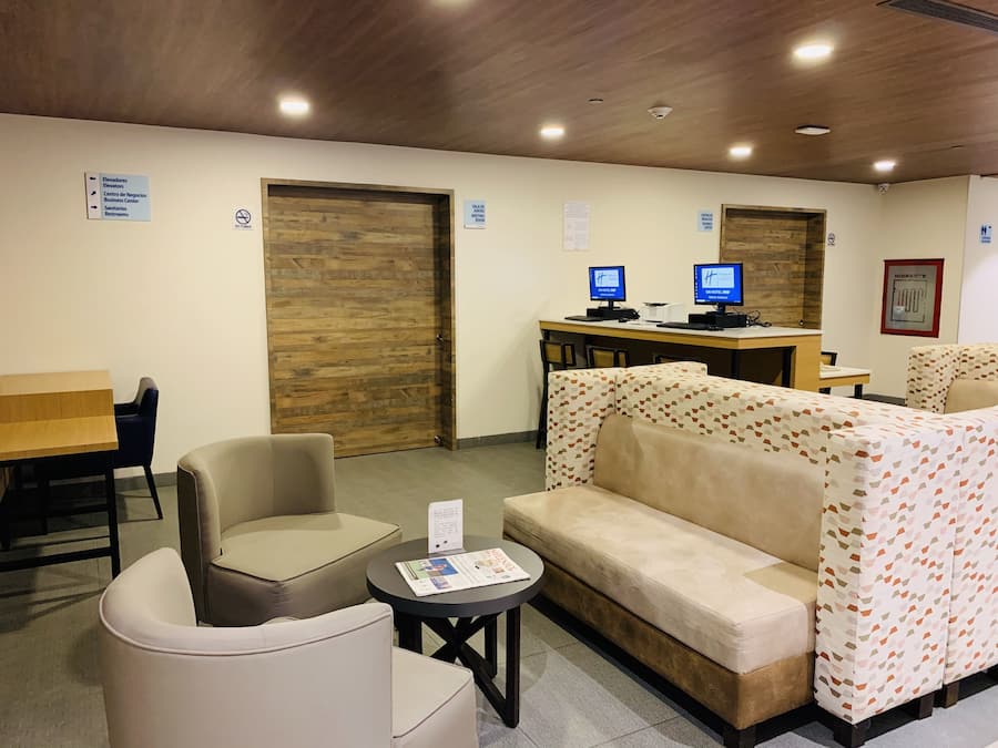 Un vestíbulo de hotel con una recepción, dos monitores de computadora, un sofá y una pequeña mesa con un menú.