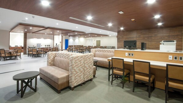 A modern dining area with multiple tables and chairs, a counter with a computer and printer, and a patterned sofa.