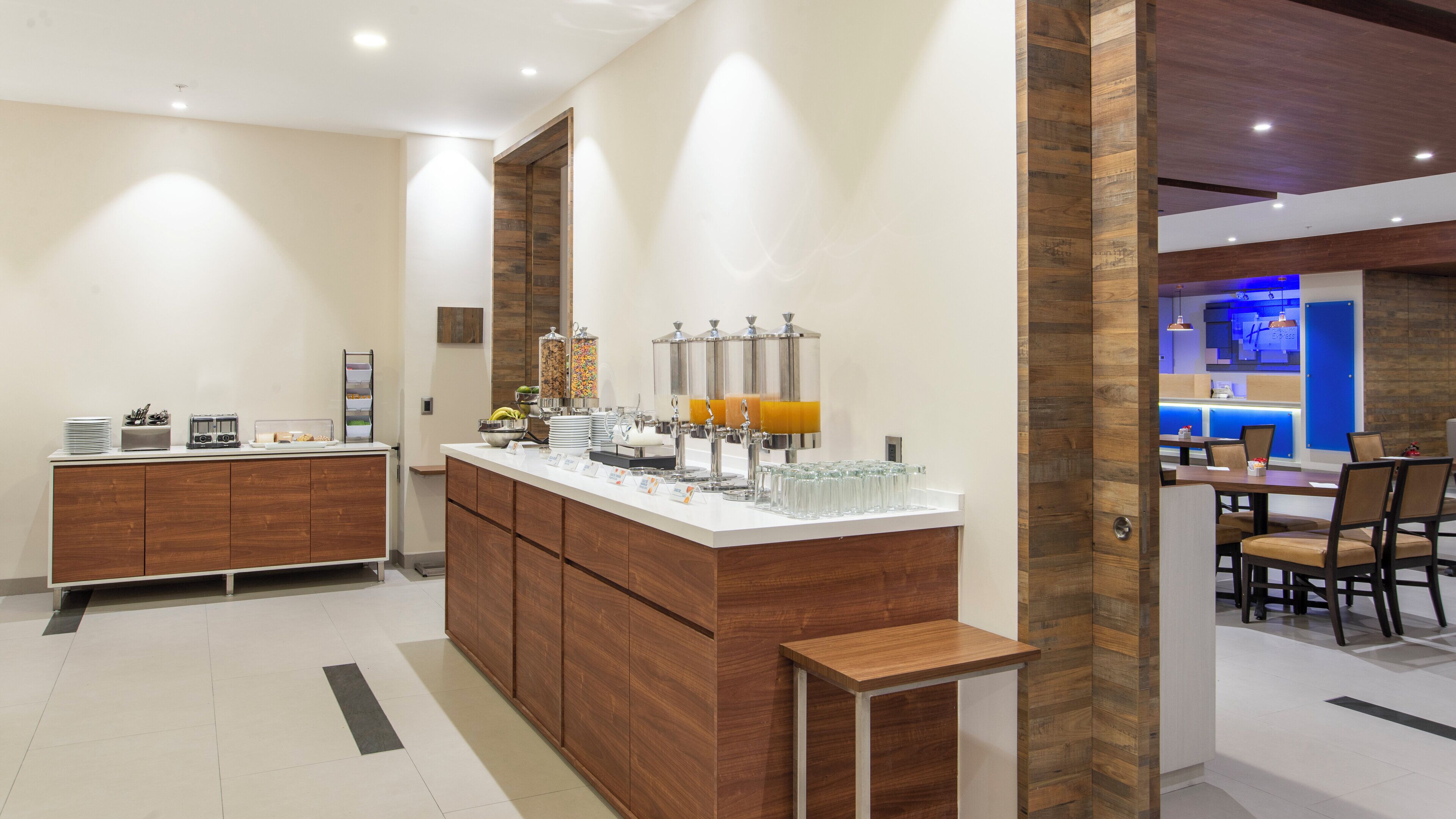 A modern kitchen area with a central island, a buffet setup, and a dining area with chairs and tables.