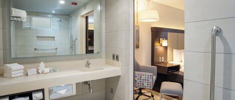 A modern bathroom with a large mirror, dual sinks, and a wheelchair-accessible chair.