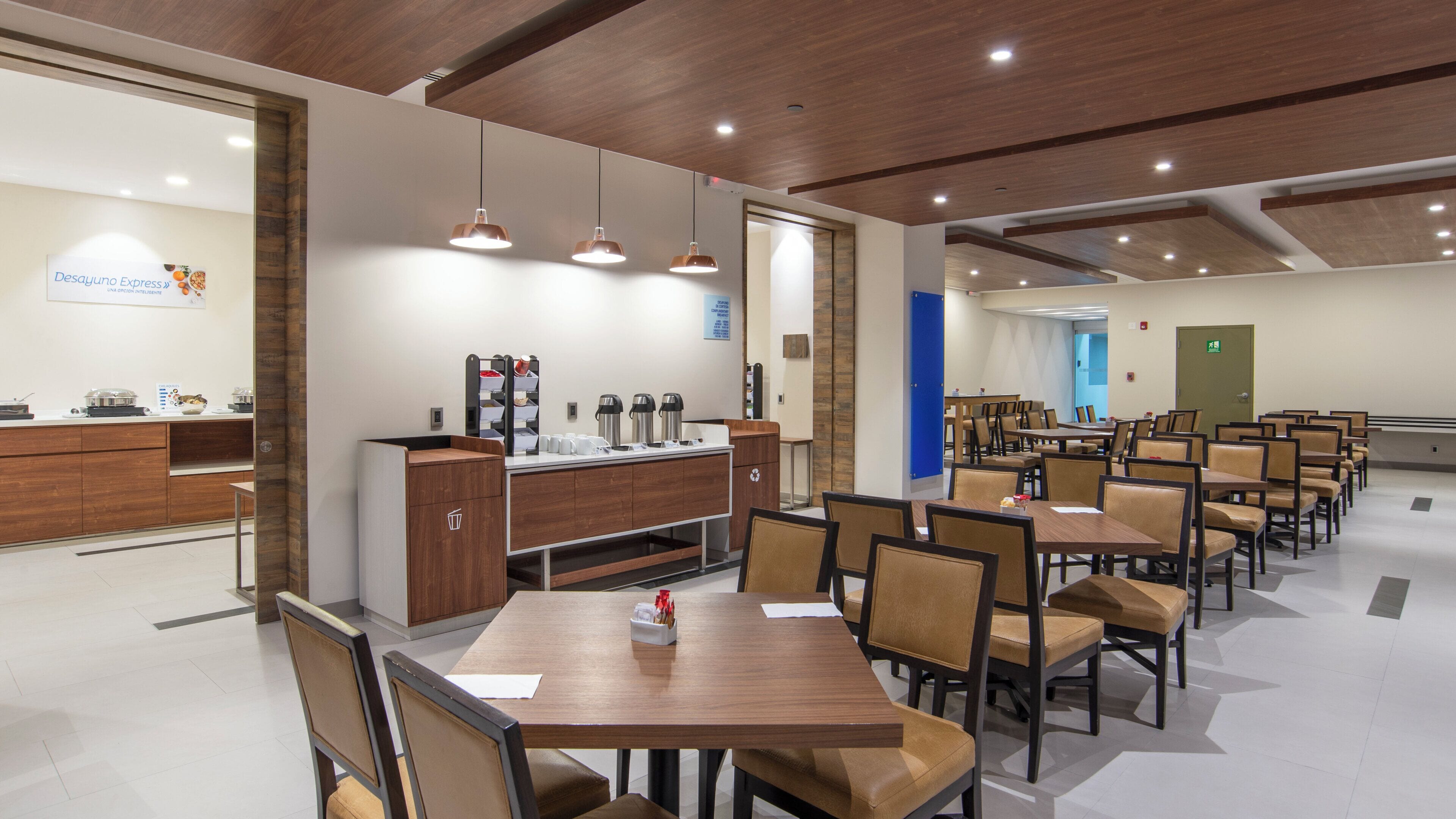 A modern dining area with wooden tables and chairs, a buffet counter, and pendant lighting.