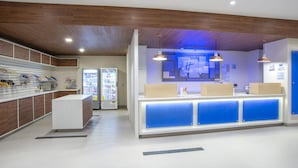 Un área de recepción moderna con techo de madera, mostrador con detalles azules y máquinas expendedoras.
