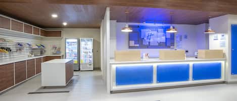 Un área de recepción moderna con techo de madera, mostrador con detalles azules y máquinas expendedoras.