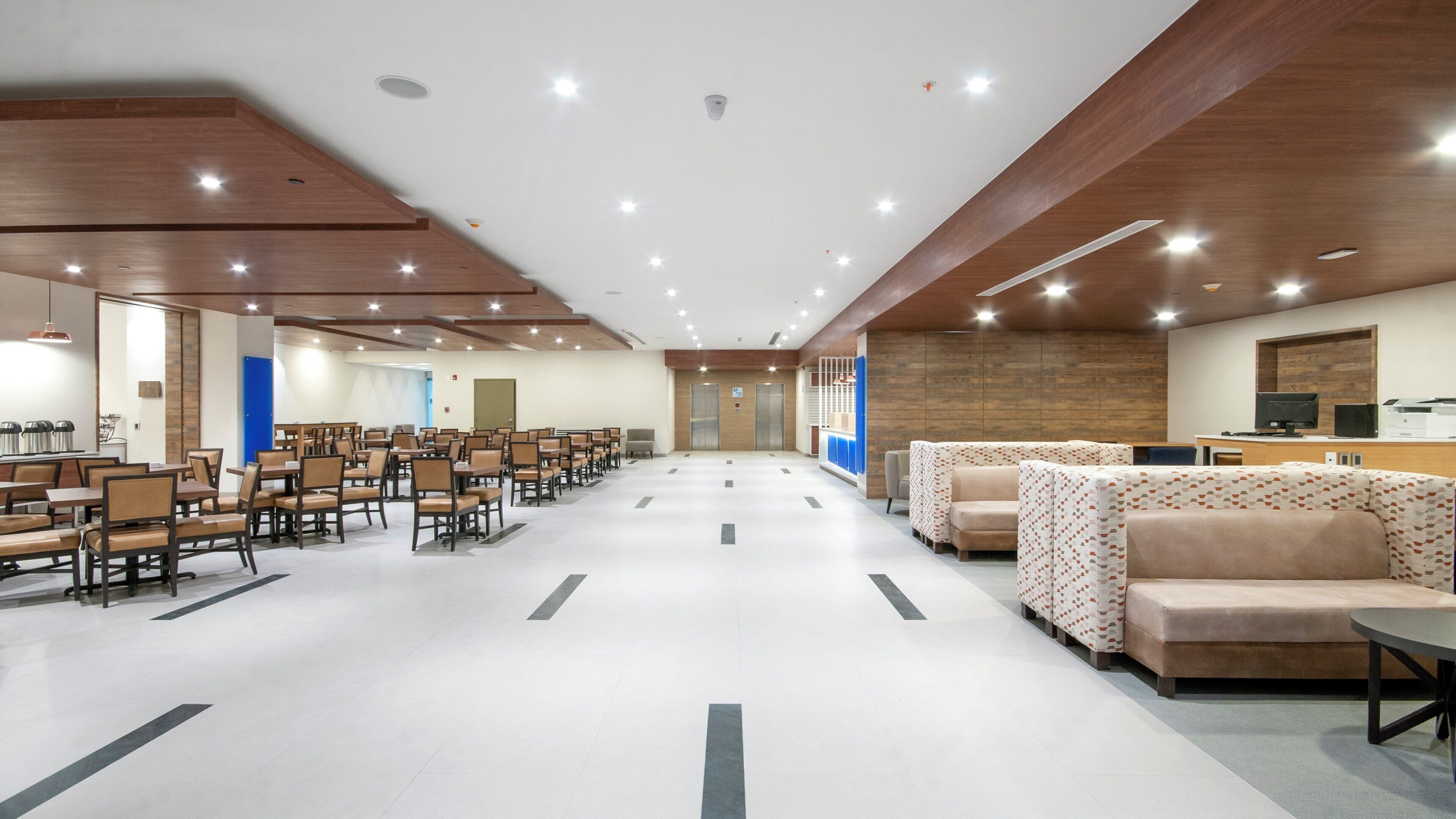 Une salle de conférence spacieuse, dotée de rangées de chaises, un espace d’accueil avec des canapés et un plafond en bois.