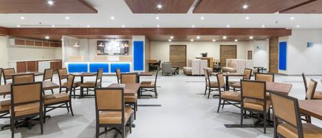 A spacious dining area with multiple tables and chairs, a reception desk, and a seating area with sofas.