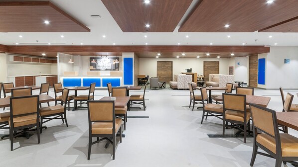 A spacious dining area with multiple tables and chairs, a reception desk, and a seating area with sofas.