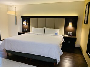 A hotel room with a large bed, two bedside tables with lamps, a headboard, and a wall-mounted light fixture.