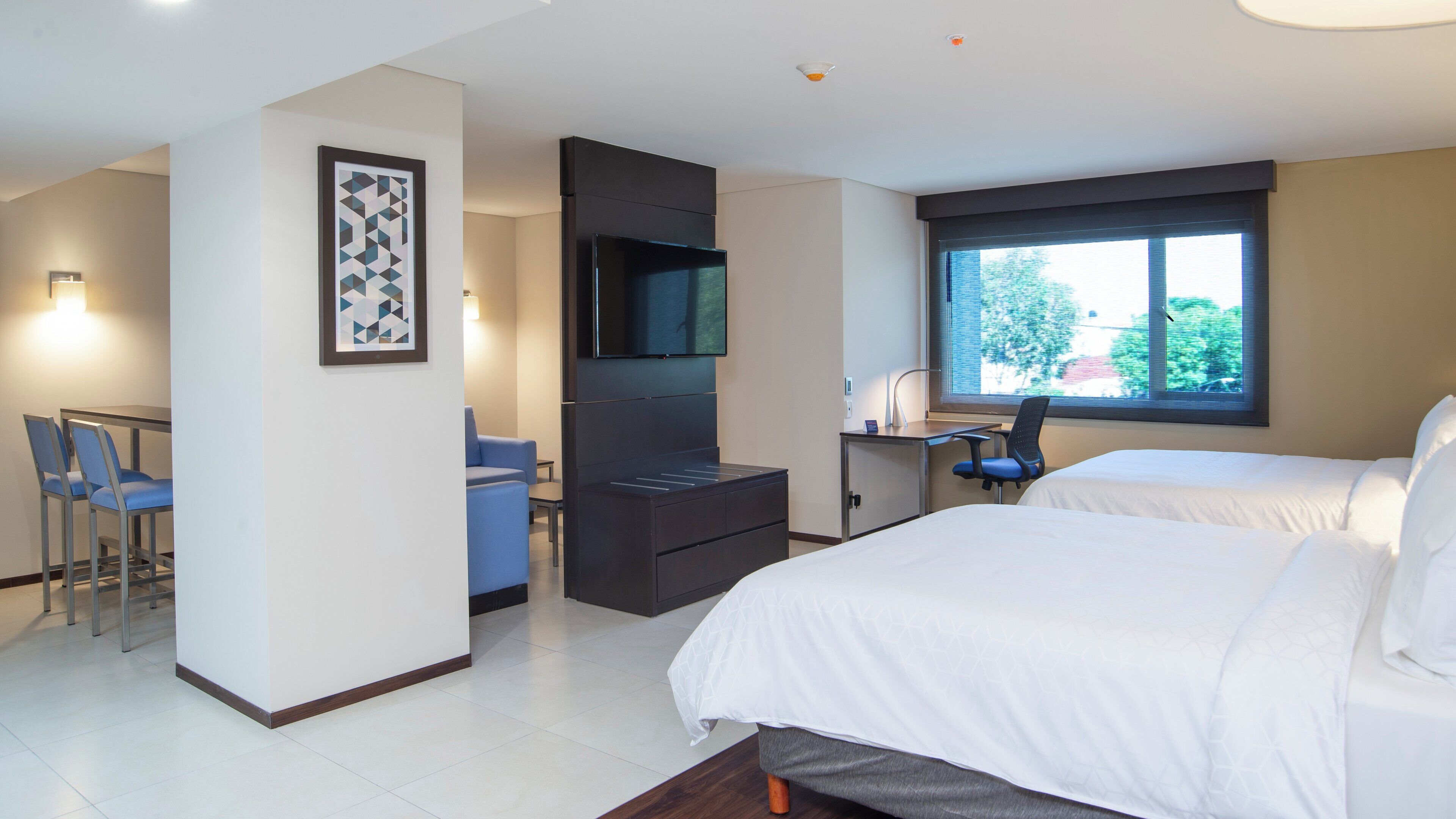 A hotel room with a bed, a desk, a chair, a TV, and a window with a view.