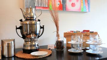 A coffee station with a samovar, cups, and a vase of dried plants.