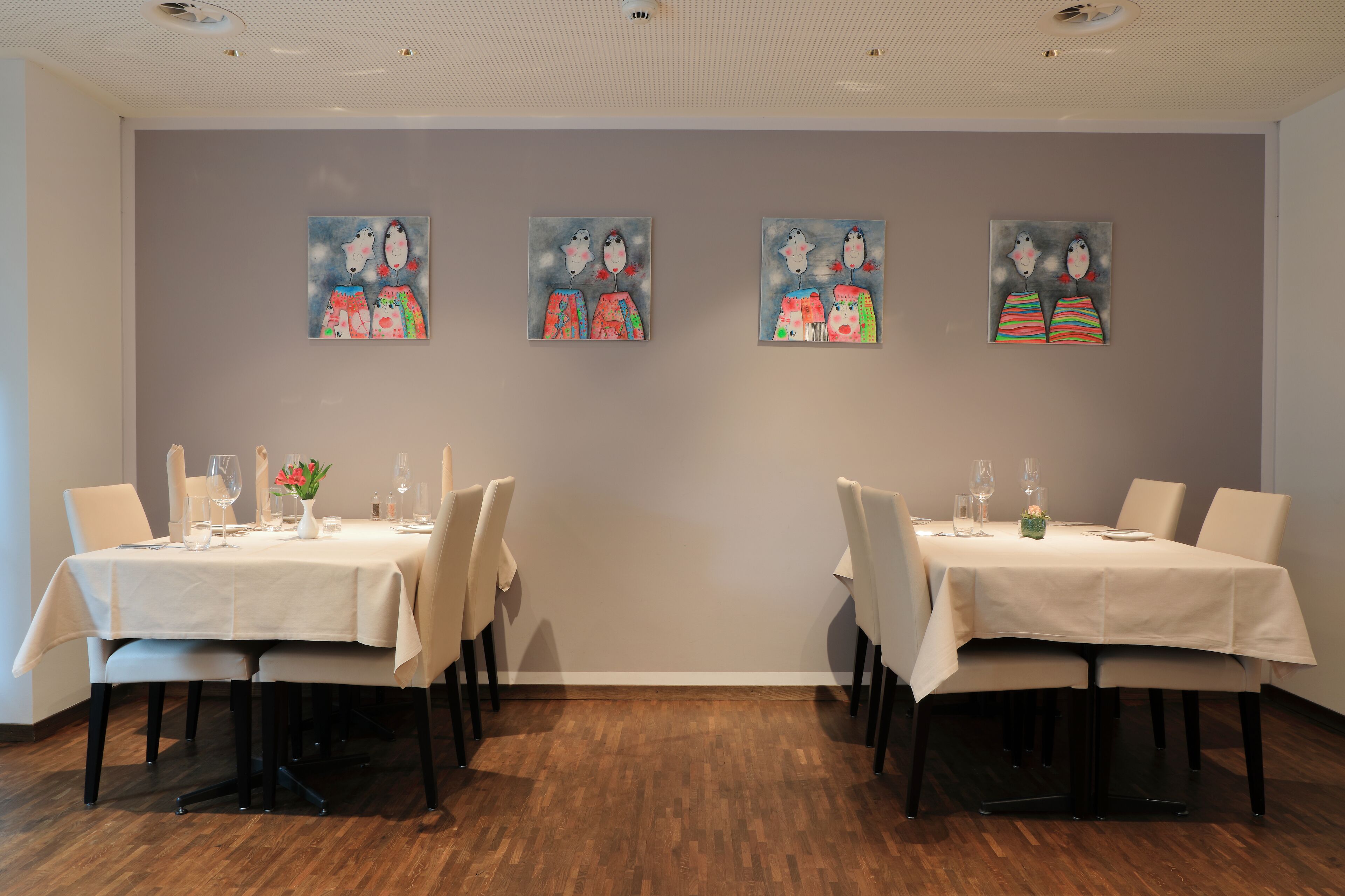 A dining area with two tables, each set with chairs, glasses, and a vase with flowers.