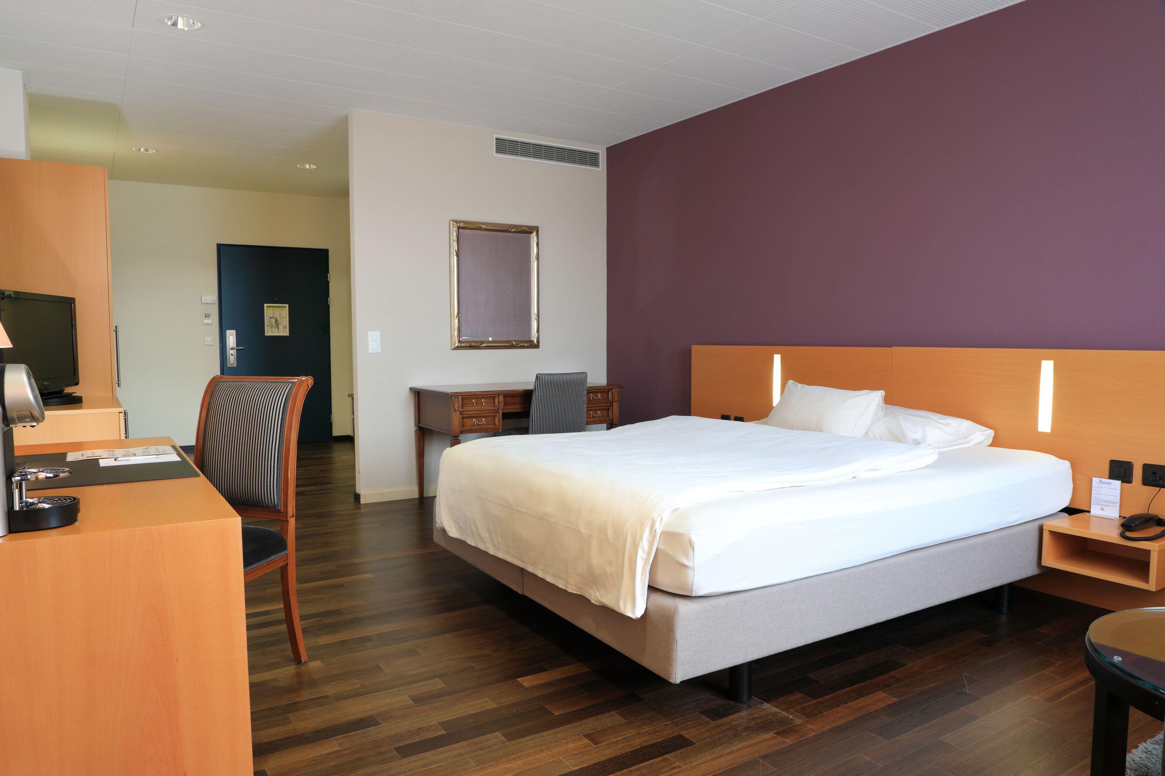 Ein Hotelzimmer mit Bett, Schreibtisch, Stuhl und Fernseher.