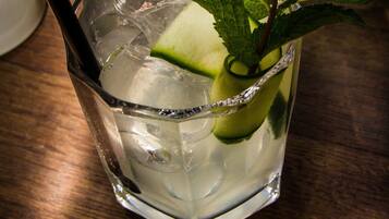 Un verre transparent contenant des glaçons, une tranche de citron vert et une feuille de menthe en guise de décoration, le tout posé sur une surface en bois.