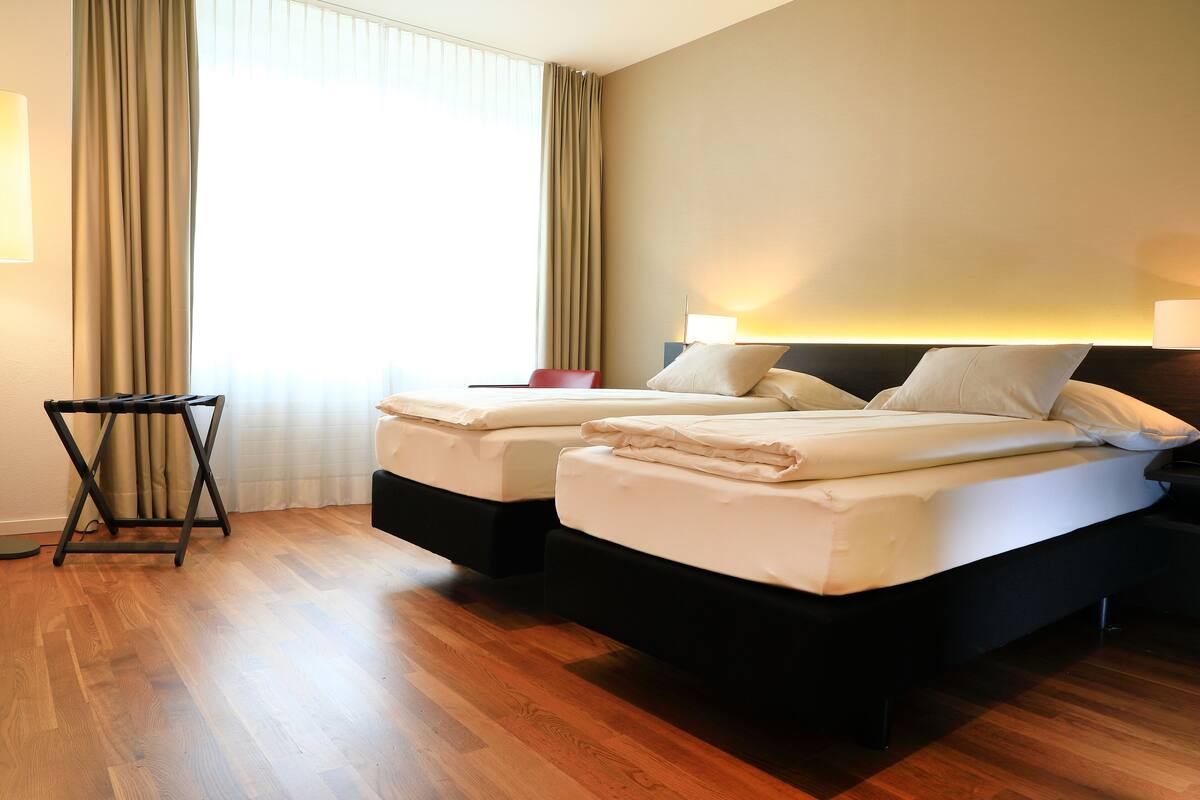 Ein Hotelzimmer mit zwei Betten, einem kleinen Tisch und einem Fenster mit Vorhängen.