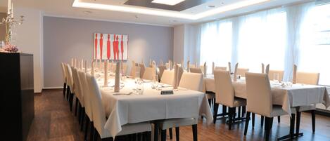 A dining area with multiple tables set for a meal, featuring a modern ceiling design and large windows allowing natural light.