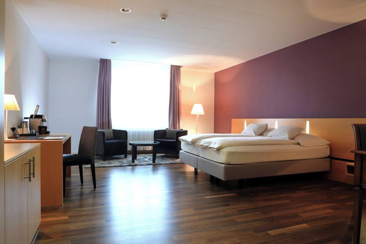 Ein Hotelzimmer mit Bett, Schreibtisch, Stuhl, Lampe und Fenster.