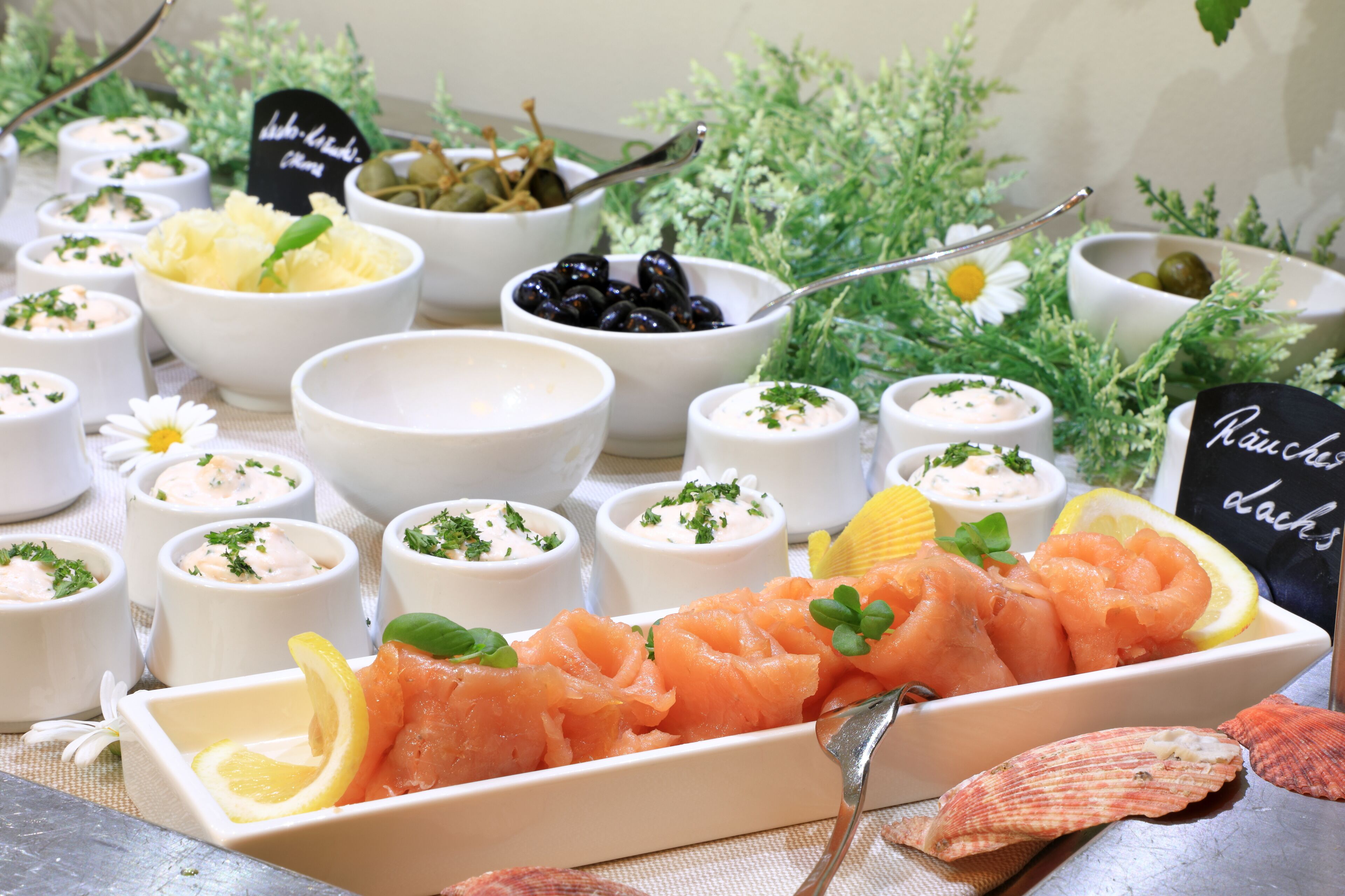Une variété de plats de fruits de mer, notamment du saumon et des olives, servis dans de petits bols et dans un plat rectangulaire, avec une pancarte indiquant « plats à la panzanese ».