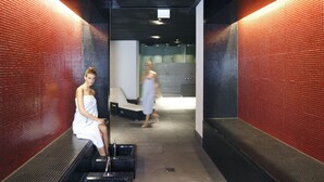 A spa area with a red-tiled wall, a bench, and a person sitting on a bench. - Hotel Banana City Winterthur (Winterthur)