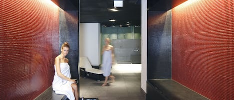 A spa area with a red-tiled wall, a bench, and a person sitting on a bench.