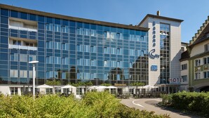 A modern hotel with a glass facade, outdoor seating area, and a sign indicating a restaurant and hotel services. - Hotel Banana City Winterthur (Winterthur)