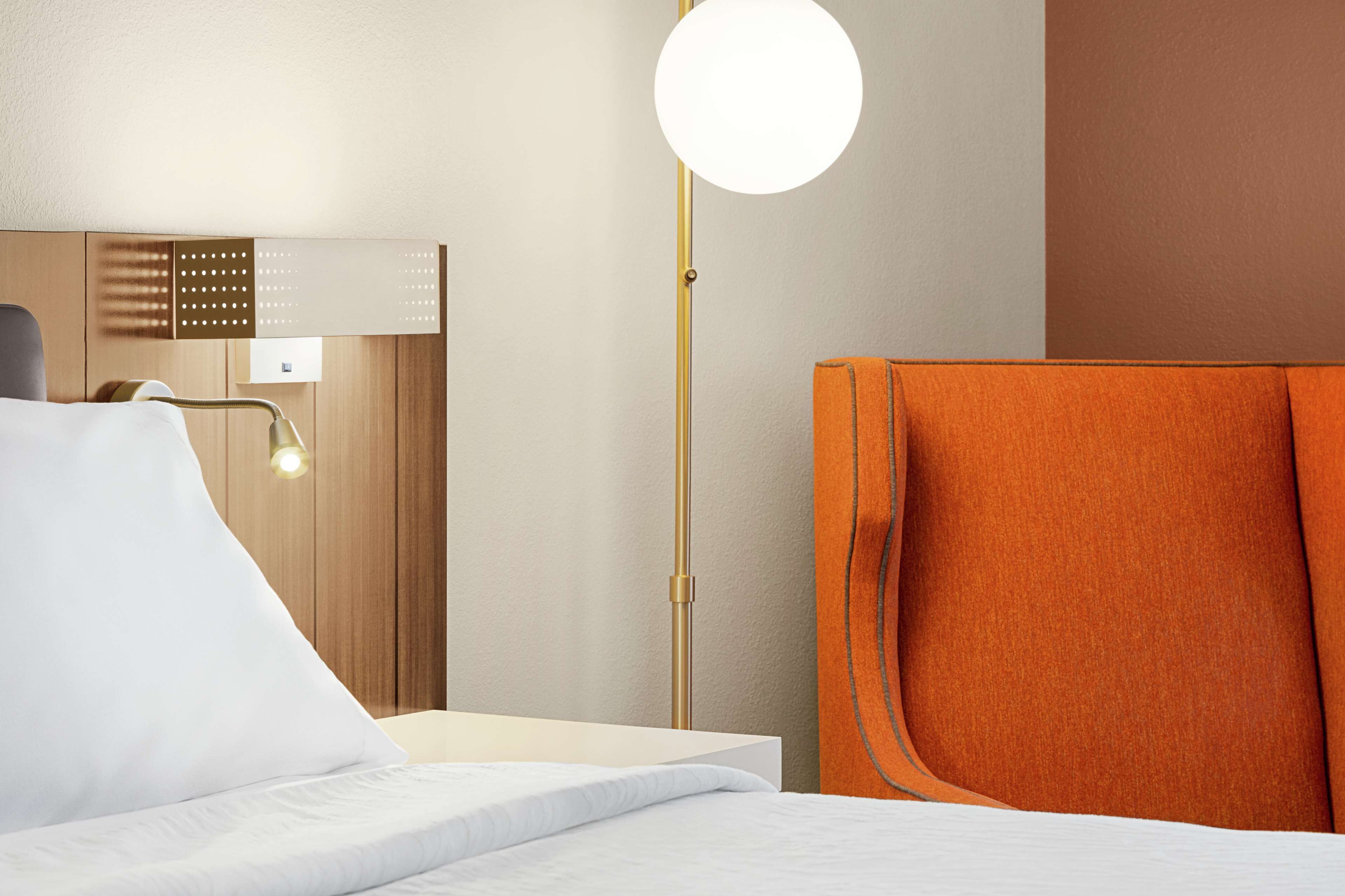 A hotel room with a bed, a nightstand, a lamp, and a wall-mounted control panel.