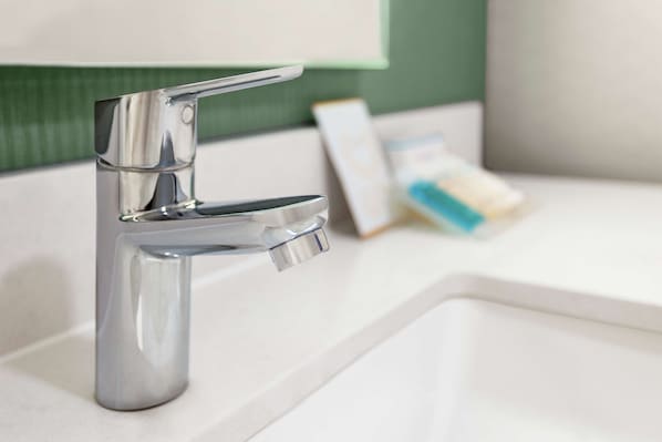 Un baño moderno con grifo cromado, lavabo blanco y pared verde.
