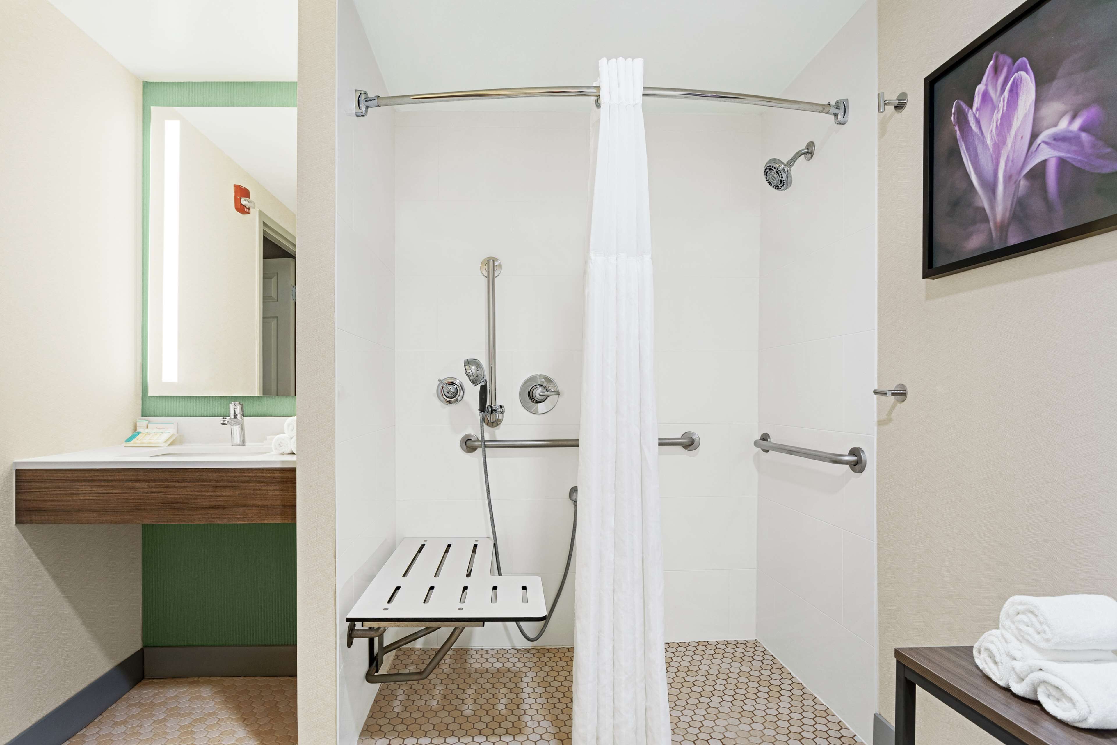 Un baño de hotel con ducha, lavamanos, espejo y toallero.