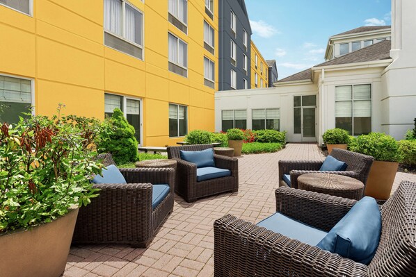 Relax in a serene outdoor space surrounded by lush greenery and comfortable wicker furniture.