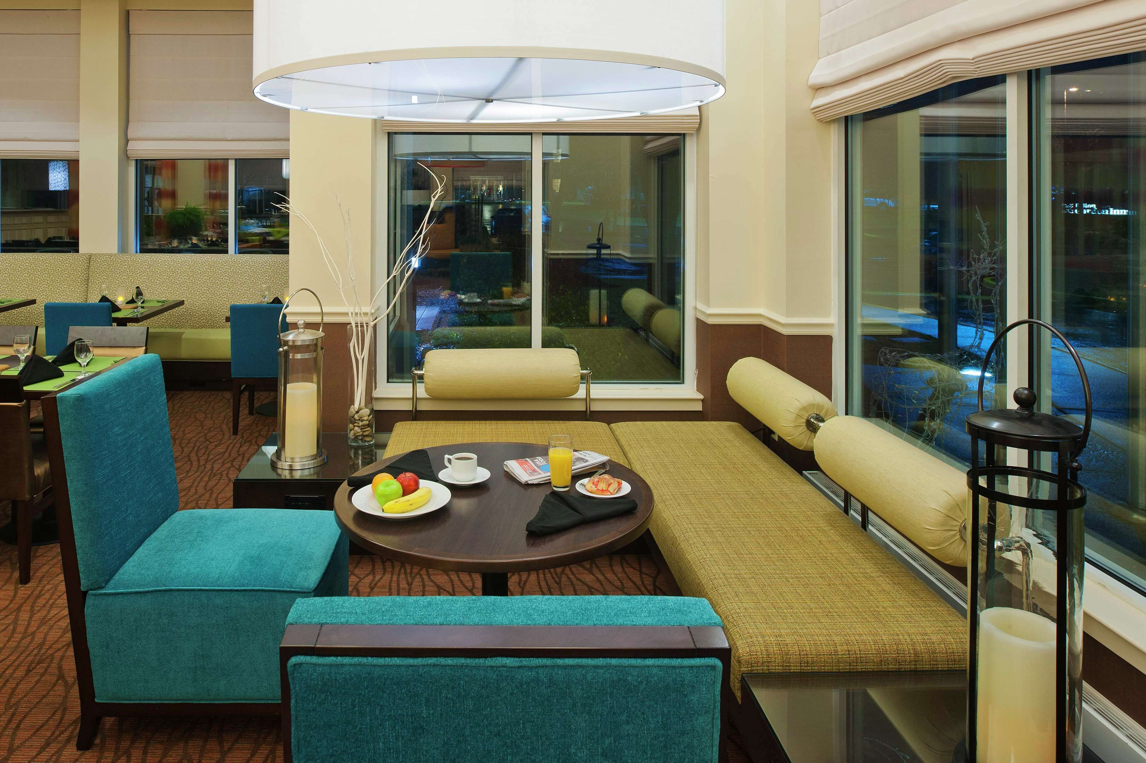 A hotel room with a dining area, a sofa, a table with breakfast, and a view through large windows.