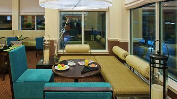 A hotel room with a dining area, a sofa, a table with breakfast, and a view through large windows.