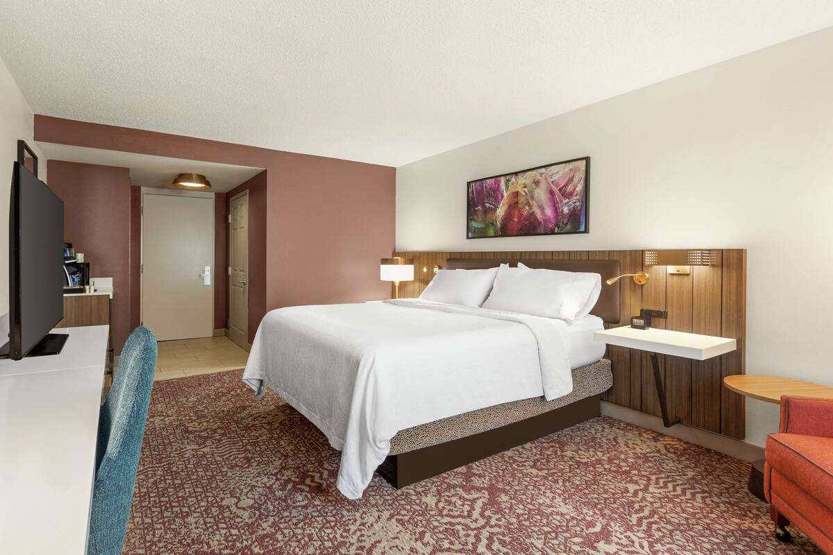 Habitación de hotel con cama, escritorio, silla, televisión y un cuadro en la pared.