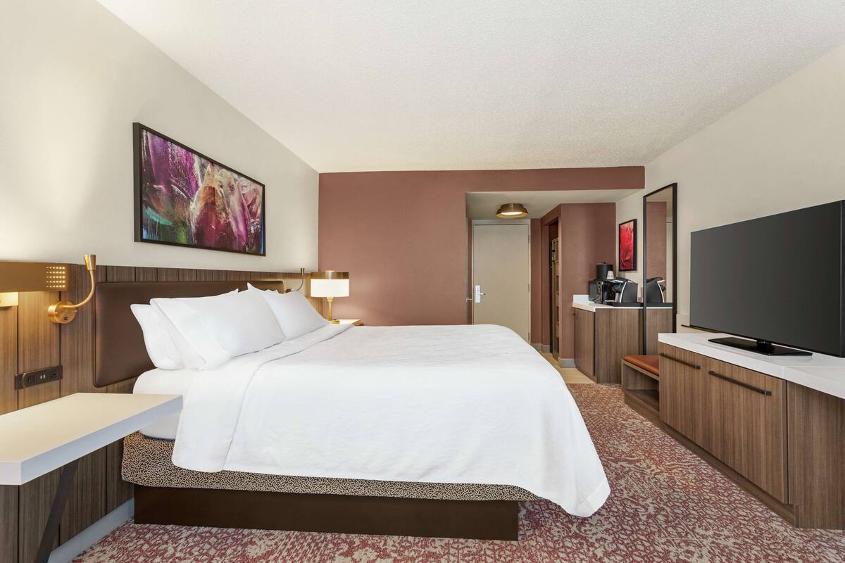 Habitación de hotel con una cama grande, un televisor de pantalla plana, un escritorio y una cafetera.