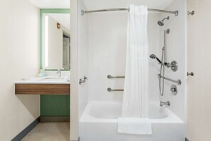 A modern bathroom with a white bathtub, a shower with a curtain, a vanity with a mirror, and a green accent wall. - Hilton Garden Inn Allentown Bethlehem Airport (Allentown)