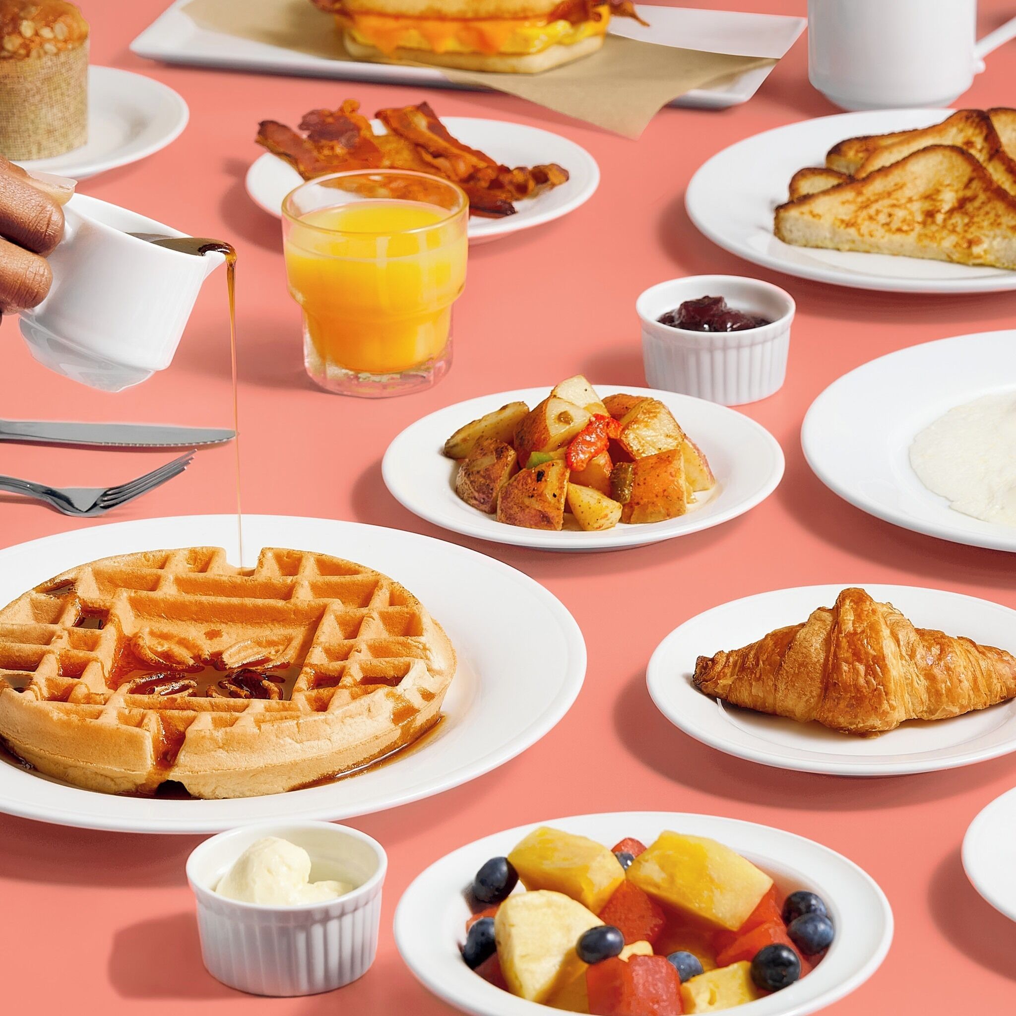 A breakfast table with waffles, croissants, fruit, and a glass of orange juice.