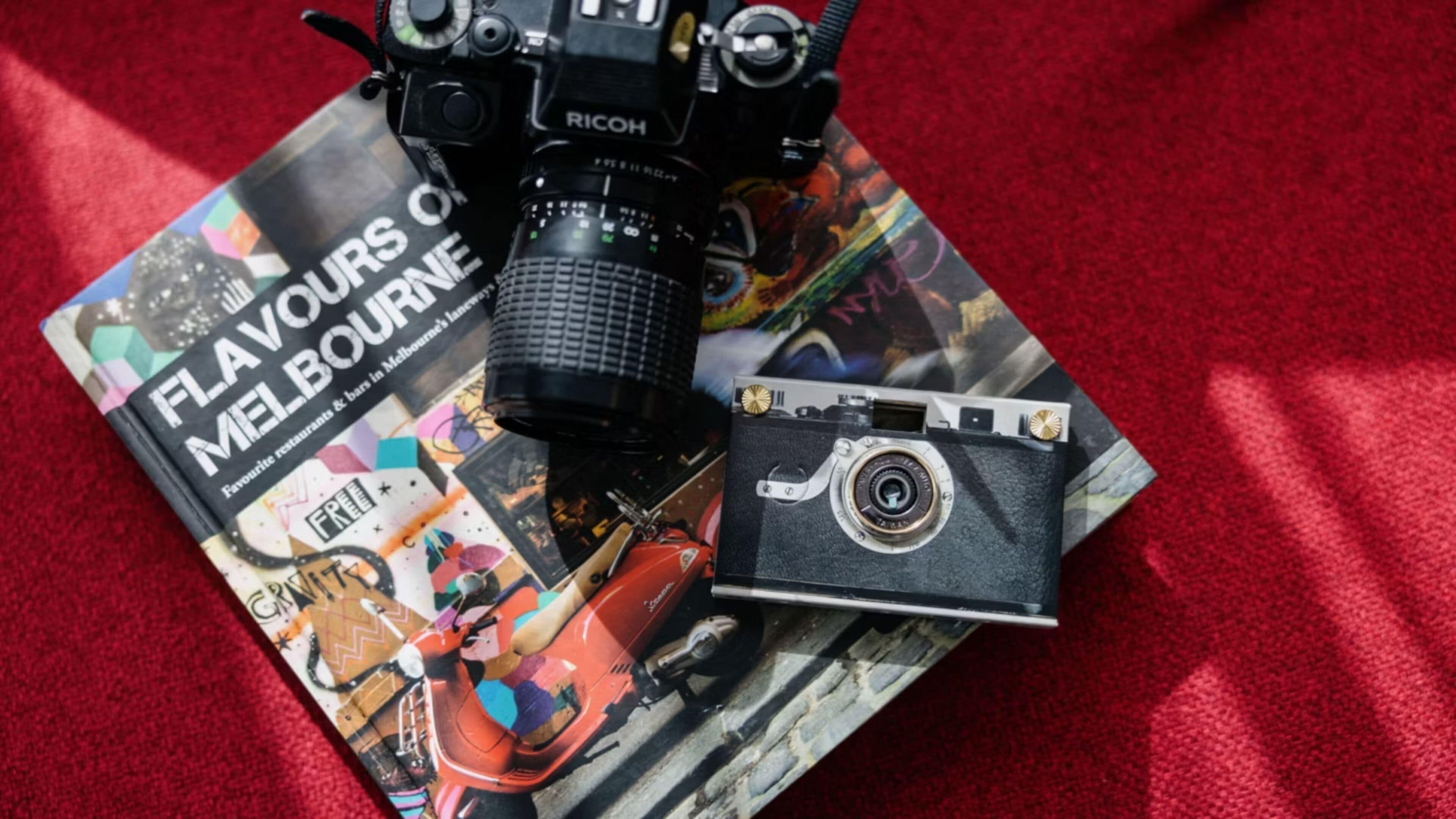 A camera on a book titled 'Flavours of Melbourne' with a red carpet background.