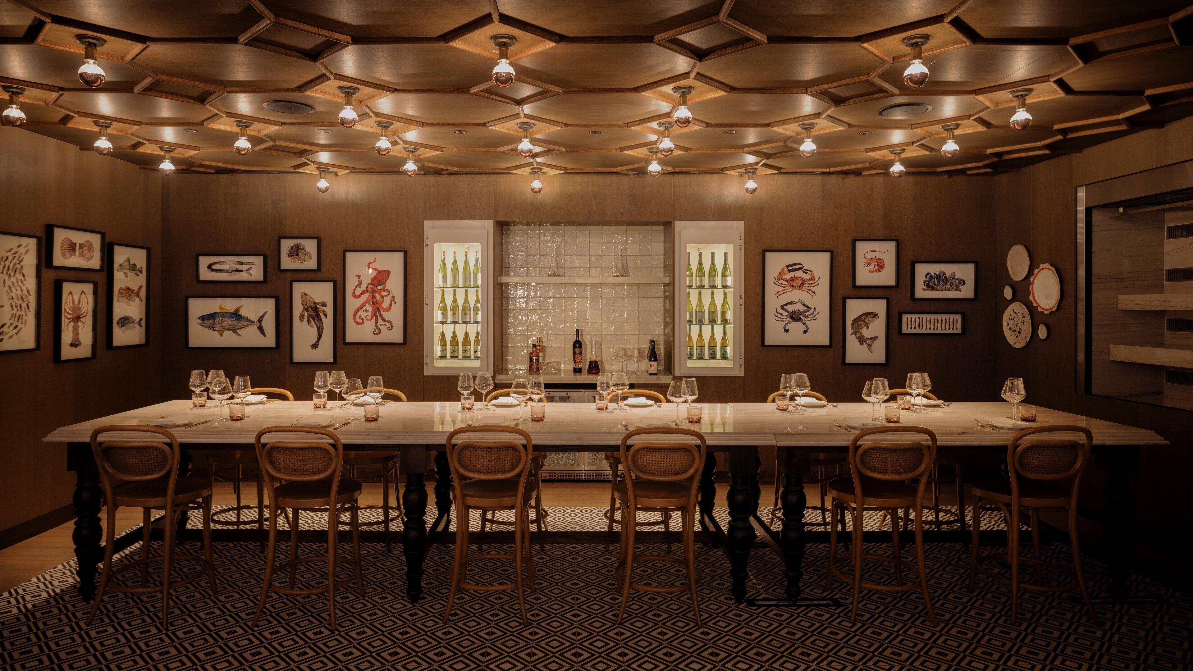 A long dining table set for a meal, surrounded by chairs, with a patterned floor and framed artwork on the walls.