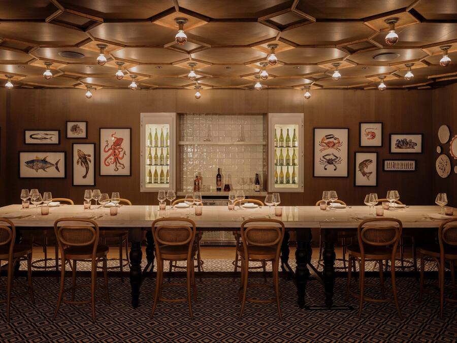 A long dining table set for a meal, surrounded by chairs, with a patterned floor and framed artwork on the walls.