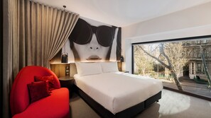 A modern hotel room with a large bed, a red armchair, a view of the city through a large window, and a unique wall art piece. - Hotel Indigo Melbourne on Flinders by IHG (Melbourne)