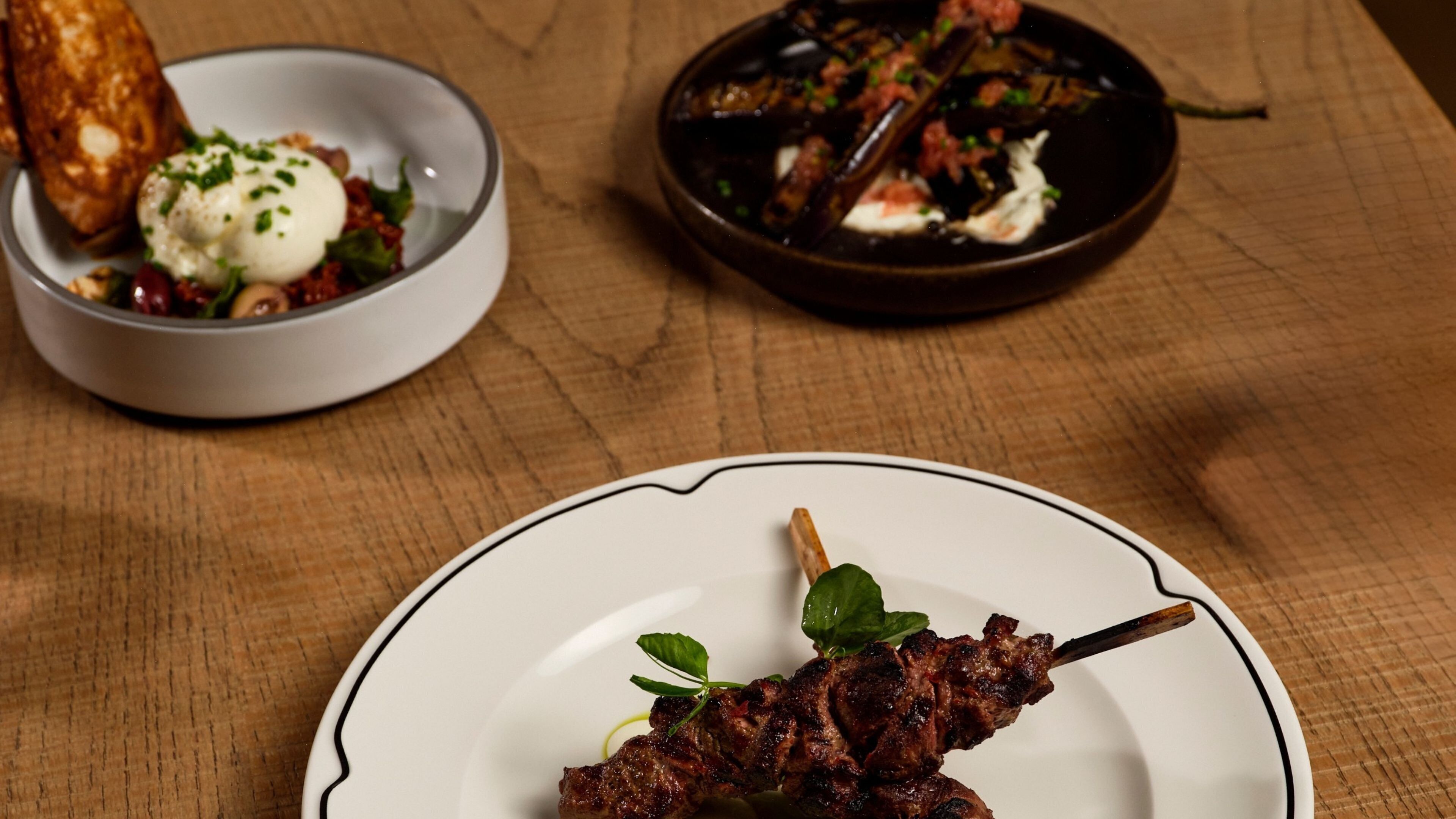 Une assiette de viande grillée en brochettes, accompagnée d’une garniture, un bol de salade avec un œuf poché, et un bol contenant un plat à base de champignons et de sauce.