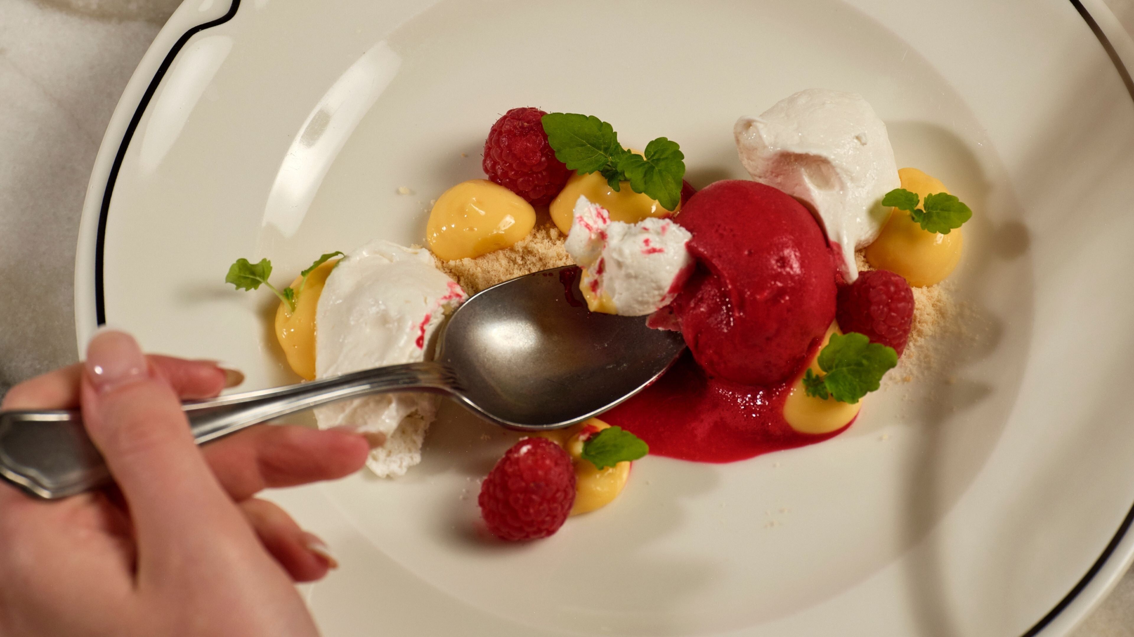 Une assiette de dessert avec de la glace, des framboises et des feuilles de menthe.