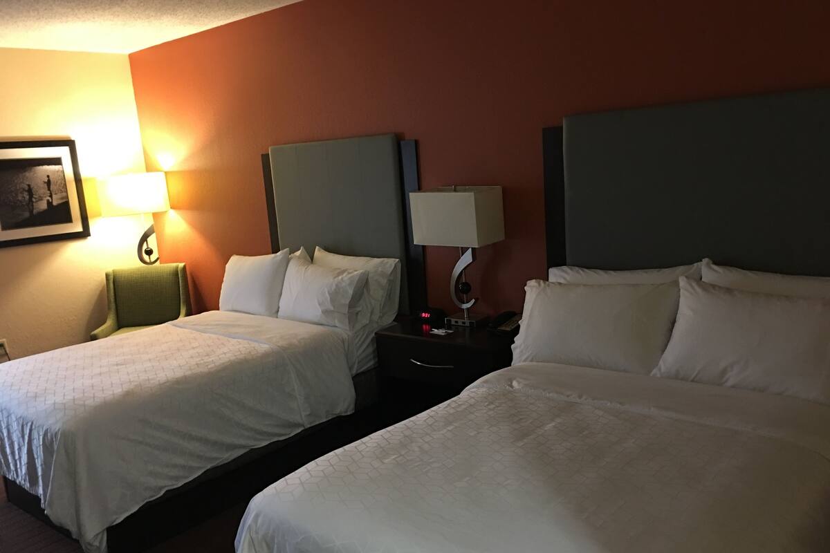 A hotel room with two beds, a nightstand with a lamp, and a framed picture on the wall.